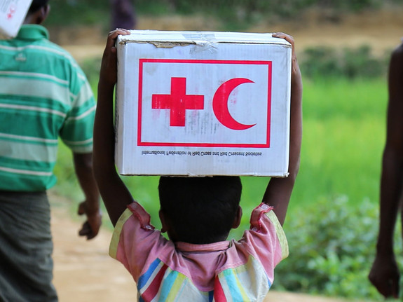 Barn som går med en kartonglåda med Röda Korsets/Röda Halvmånens logga på. Foto: Mostphotos
